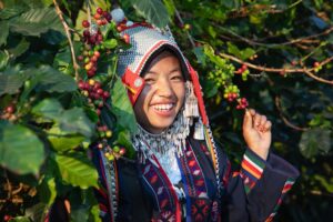 Smilende person iført traditionel dragt ved busk med bær.