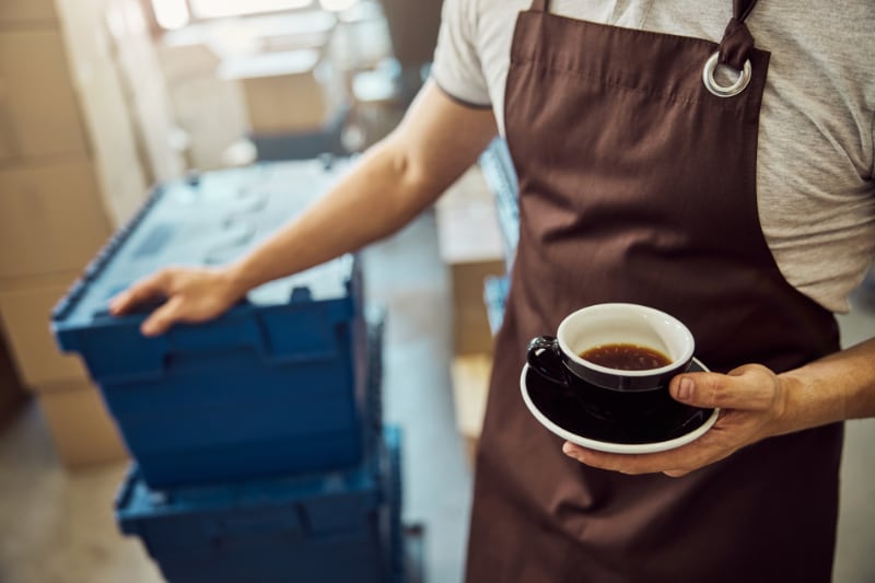 Mand i forklæde holder kaffe.